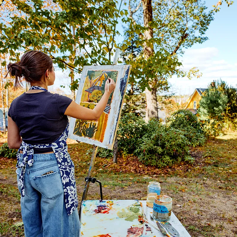 A student at an easel paints the surrounding fall landscape.