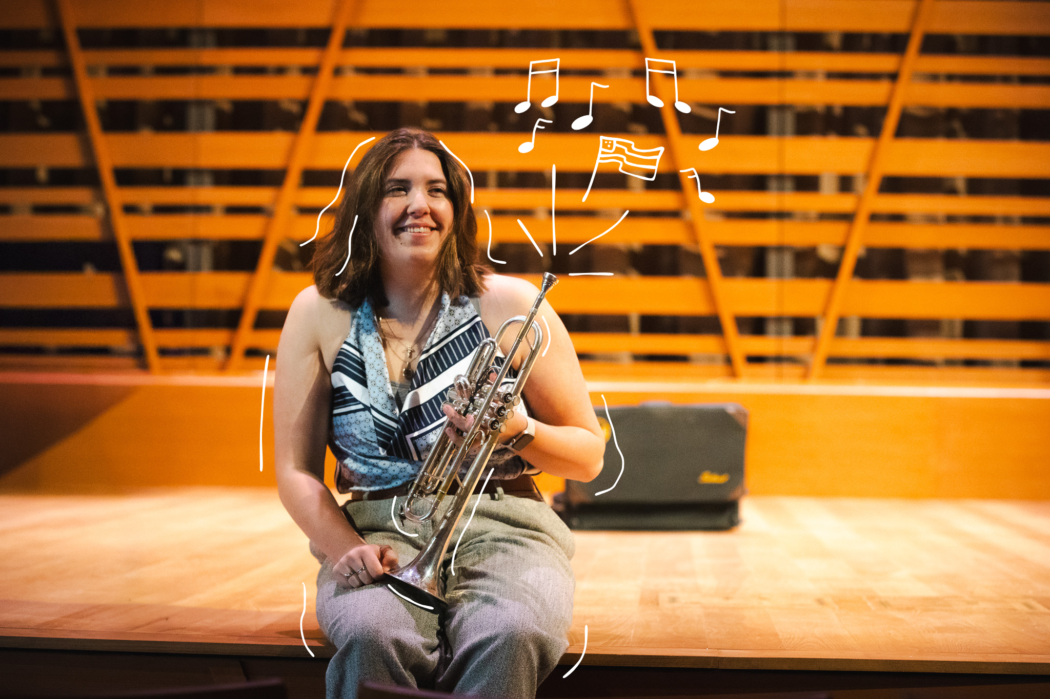 Hannah Paterson smiles while holding her trumpet on the Crewe Center's stage, with illustrated music notes and an American flag floating around her.