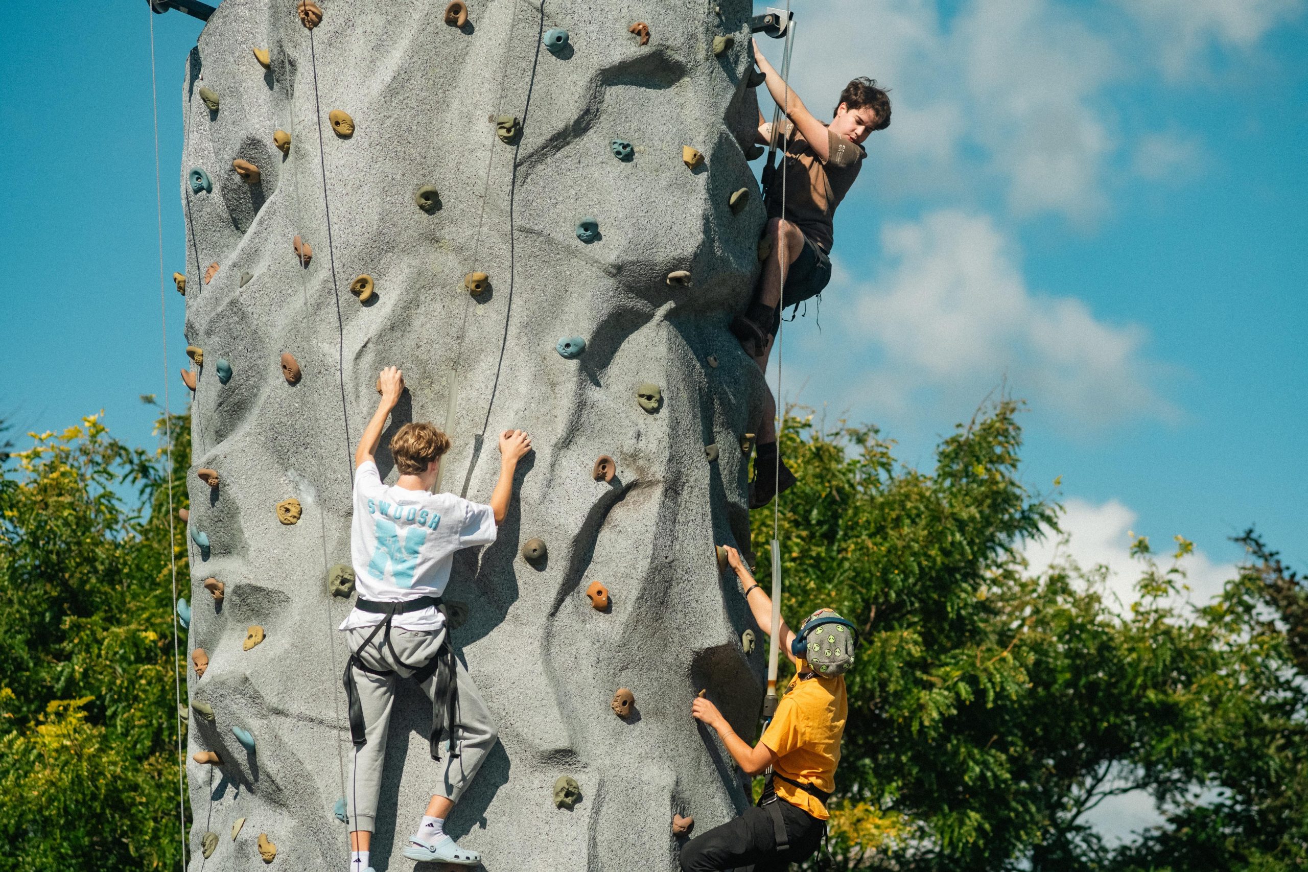 USM students climb a rock wall together outdoors during Fall Fest, part of Homecoming Weekend.