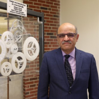 Dr. Mehrdaad Ghorashi stands beside a mechanical clock built by one of his students.