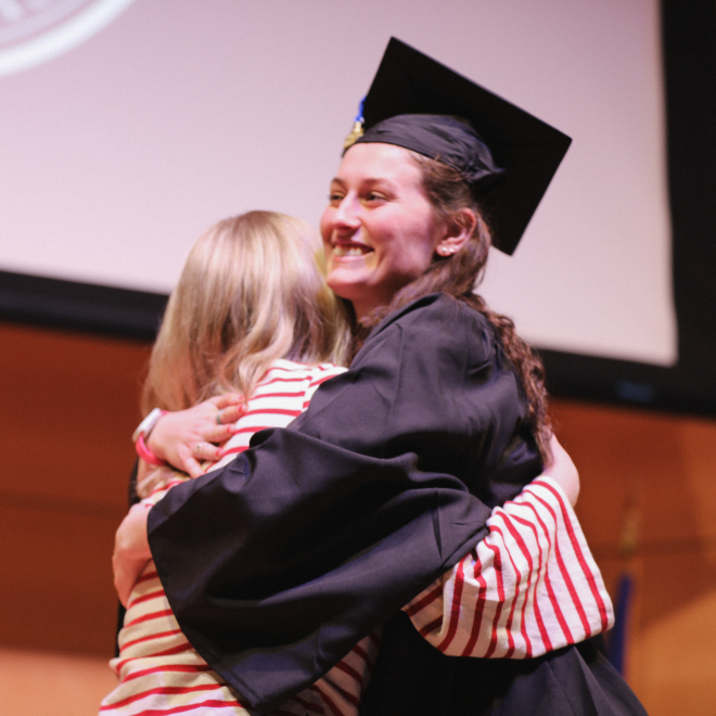 USM nursing graduate hugs friend on stage of pinning ceremony