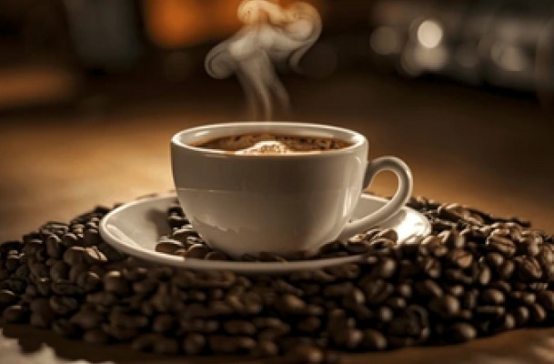 A cup of steaming coffee siting on a pile of coffee beans.