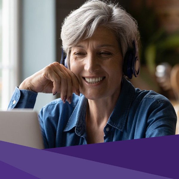 A woman with headphones on smiles while watching a laptop screen