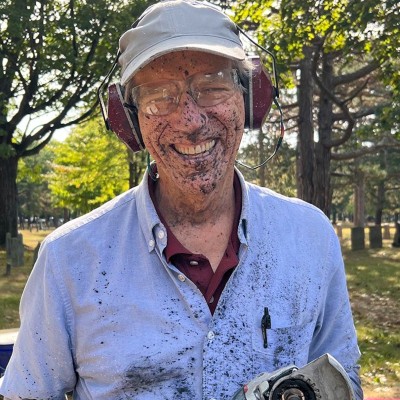 Jonathan Monroe wearing goggles and ear protectors laughs after being sprayed with mud