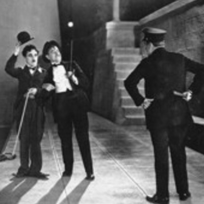 Two men in formal attire stand with a police officer on a sidewalk at night.