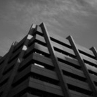 A low-angle, black and white shot of a modern building with many horizontal lines against a sky with wispy clouds.