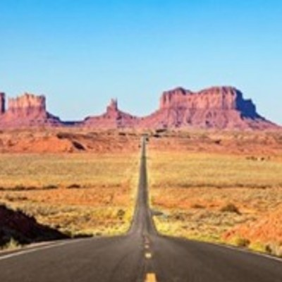A long, straight Route 66 leads through a desert landscape towards the iconic buttes of Monument Valley.