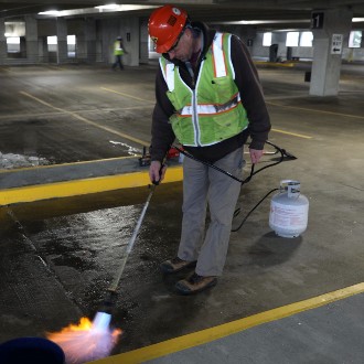 A blowtorch readies the pavement for directional markings to guide drivers through the new traffic configuration.
