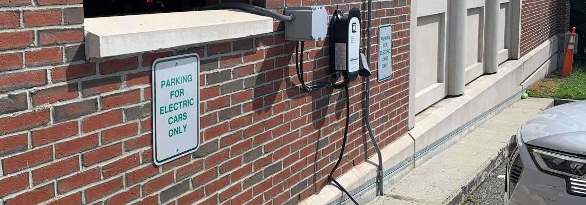 Electric vehicle charging station on the wall outside the parking garage, with a cord running to an electric car.