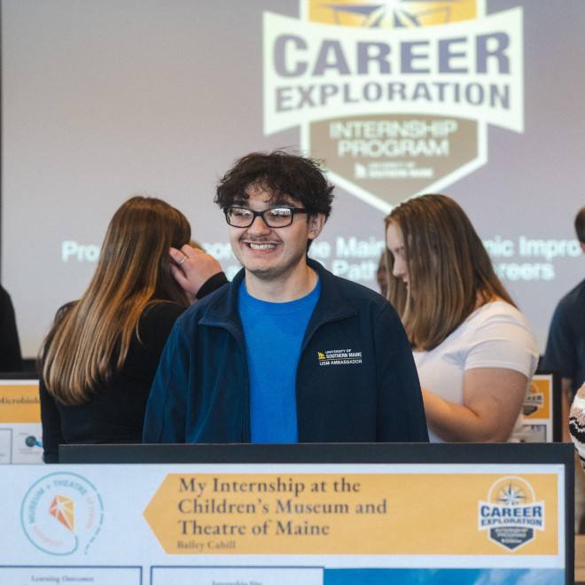 A USM Career Hub Ambassador smiles at the Career Exploration Internship Program''s poster exhibition.