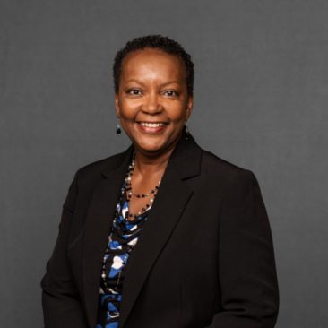 Photo of Idella Glenn. Idella is a Black woman of Afro-American heritage with brown hair and brown eyes. She is wearing a black jacket and is smiling.