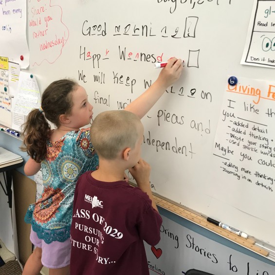 Two elementary students working at whiteboard in classroom