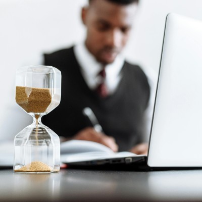 man writing and typing with hourglass in the foreground