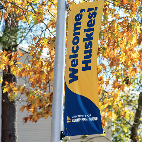 A banner that reads, Welcome, Huskies! and features the USM logo hangs from a light post on campus.