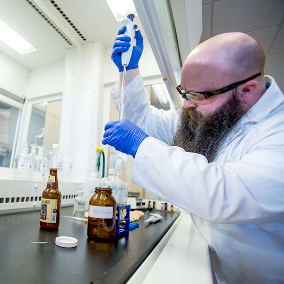 A long-bearded student wearing safety goggles transfers liquid into a set of test tubes in one of our chemistry labs.