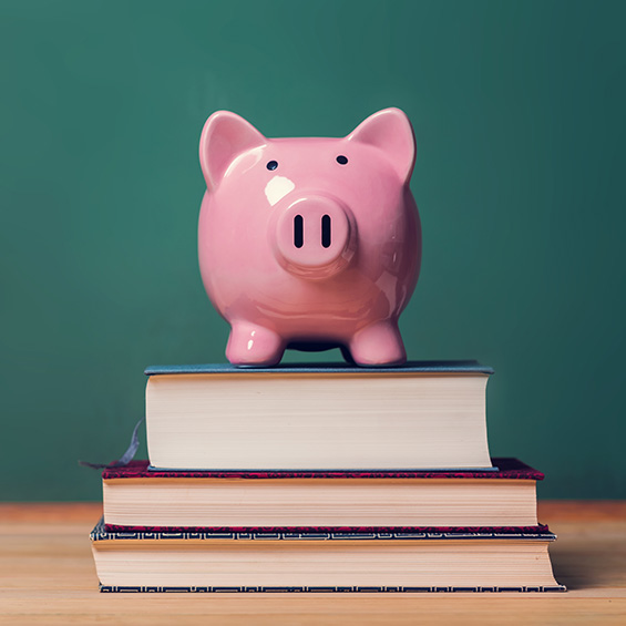 A piggy bank perched on a stack of three books in front of a dark green wall.