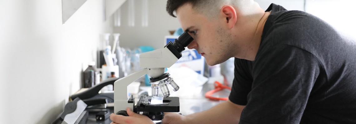 Young man looks through microscope on a lab bench