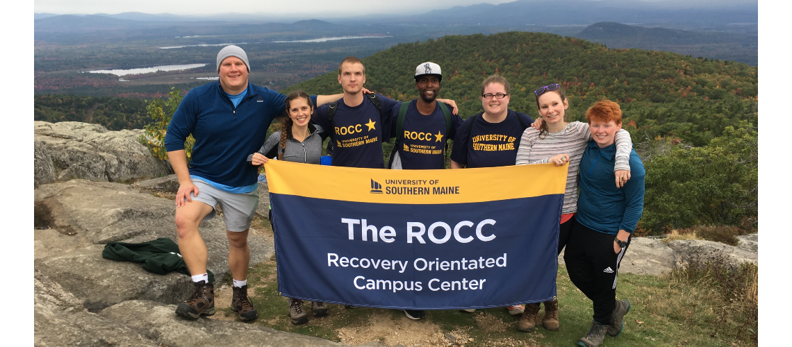 a group of students and staff of The ROCC on a hike and holding up a ROCC flag