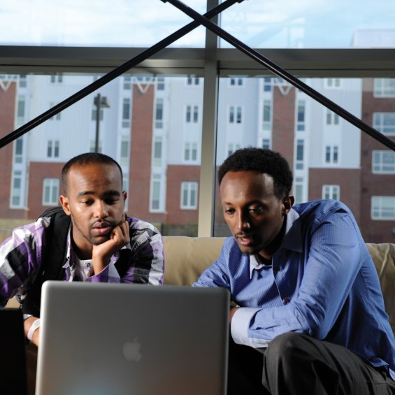 Two students intensely regard a Apple laptop. It appears that they are discussing something.