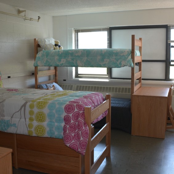 Picture of residence hall room with 3 beds with colorful bedspreads. Two of the beds are bunked. 