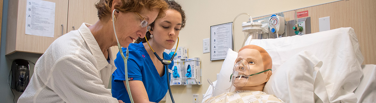 Nursing instructor and student examine simulation patient in lab.