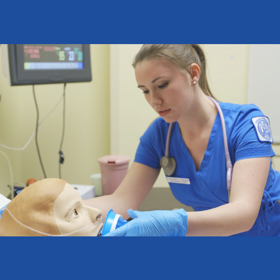 Nursing student applies oxygen mask to simulation mannequin. 
