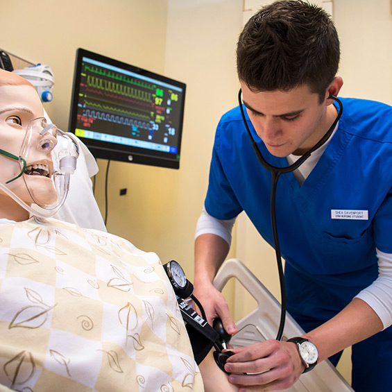 A student practices taking blood pressure on a simulation mannequin.