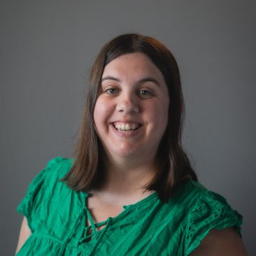 A headshot of Lindsay. She has shoulder length brown hair and a green top.