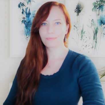 This is a photo of Netty Provost. She is facing the camera wearing a blue long-sleeved top and smiling slightly. She has long red hair.