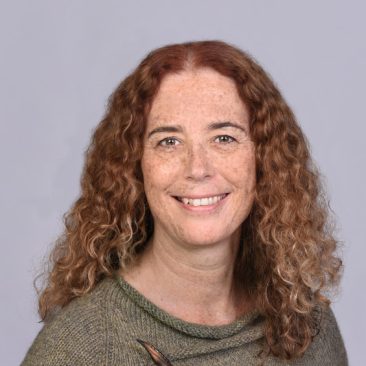 Catherine Lyden, wearing a green top against a grey background.