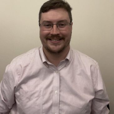 Tim is wearing glasses and a striped shirt and is smiling.