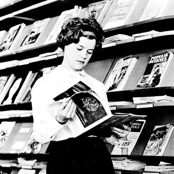 A young person standing reading a periodical
