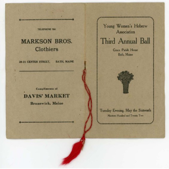 A tan color pamphlet facing downward open to show the front and back cover  with a red tassel attached to the middle of the spine that hangs downward.