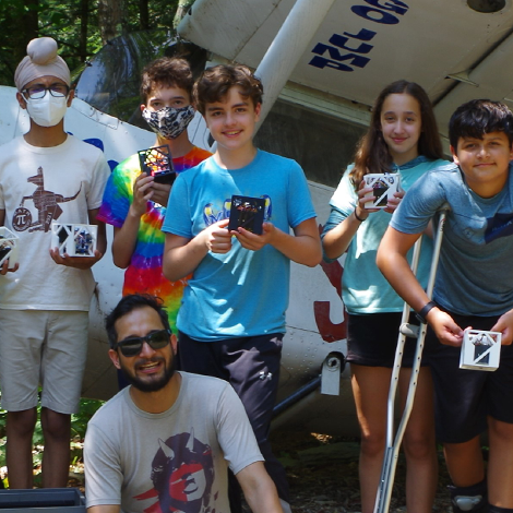 Campers and instructor posing in front of plane and holding CubeSats.