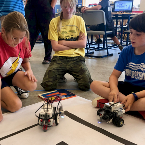 Campers sitting around mission board watching two LEGO robots navigate.