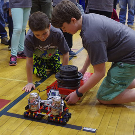 Two participants attaching a competition LEGO robot to a cart of weights at an RTMA event.
