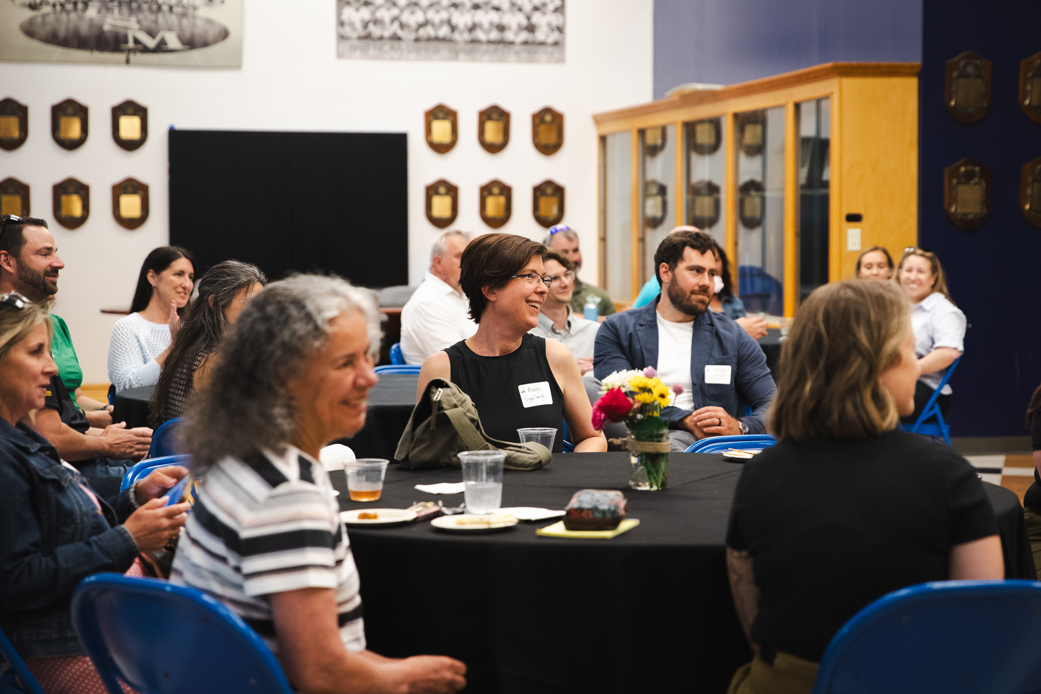 Attendees seated at round tables laugh and chat during the "Good People, Great Connections" networking event at USM's Alumni Reception Center, with championship plaques lining the walls behind them.