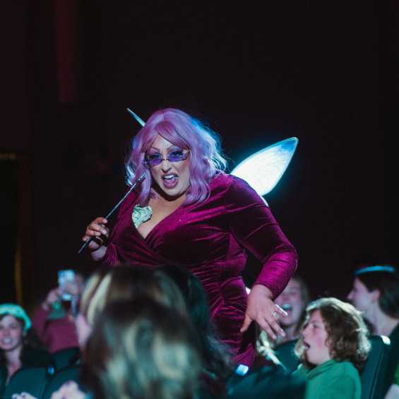 Drag artist in Shrek Fairy Godmother outfit performing among audience members