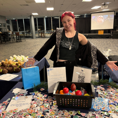 SEAB Student Staff member smiling with arms outstretched behind table with prizes for an event