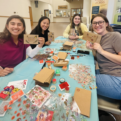 Four students smiling and holding up hand-made cards at a table