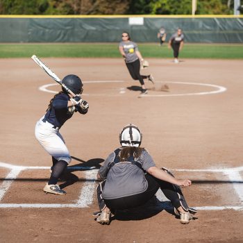 A pitcher throws a softball as a batter stands in position at an alumni softball game.