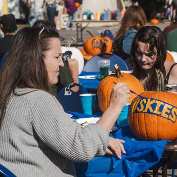 An Octoberfest attendee painting the word "Huskies" on a pumpkin.