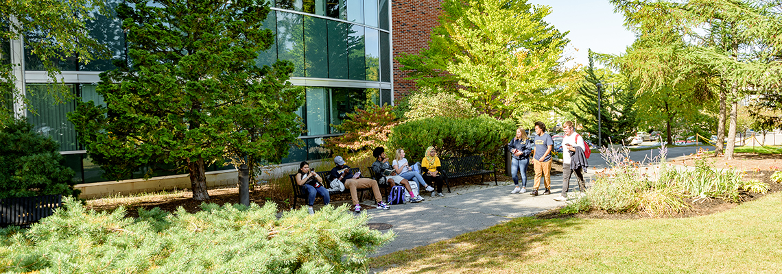 Students sit on benches and walk on a sidewalk outside on campus.