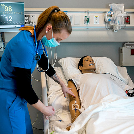 A nursing student checks the vital signs of a simulation lab dummy.