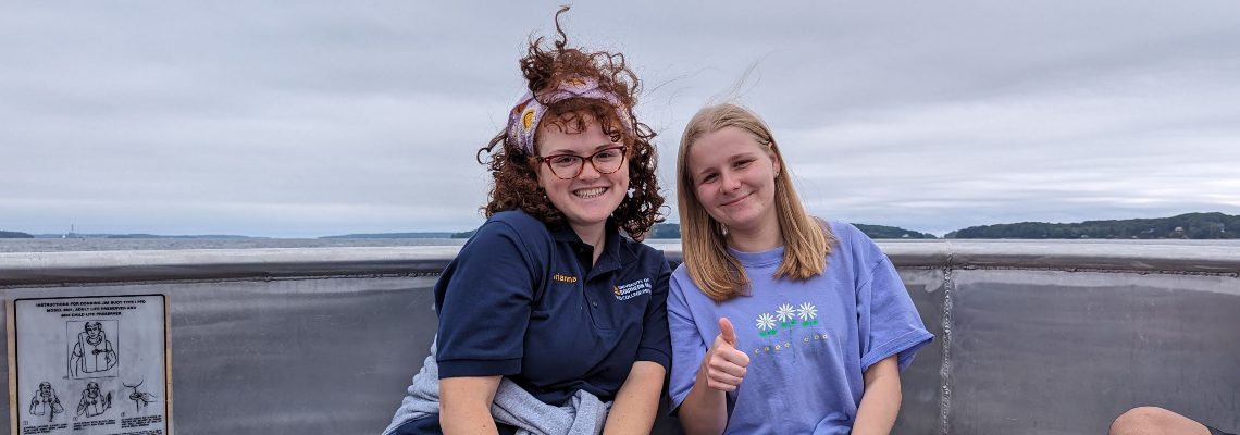 Two students sitting on a ferry smiling at the camera