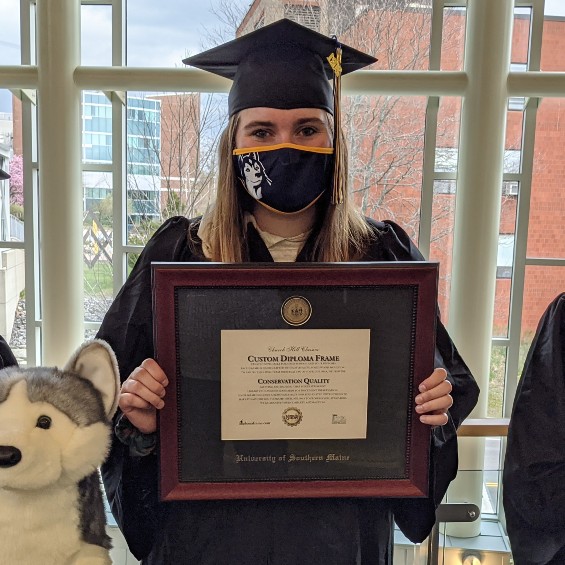 A student holding a diploma frame next to a stuffed husky