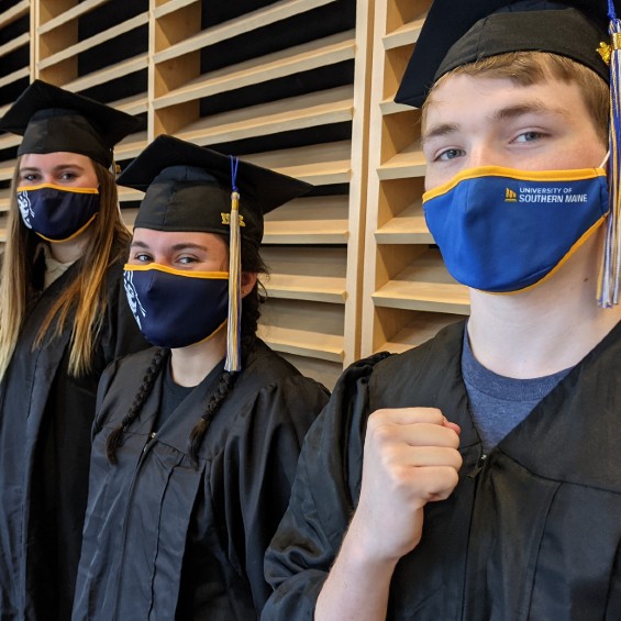 Three students standing in a row in graduation regalia