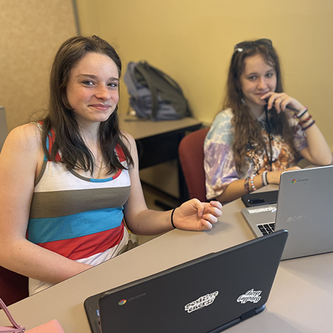 two girls smiling behind laptops