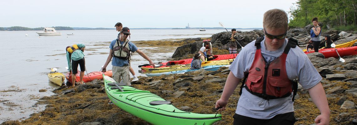 Two students each holding the end of a kayak on a beach