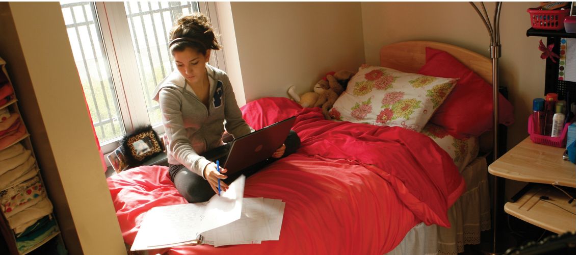 student doing homework with a laptop and binder in their bedroom